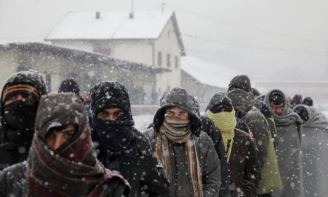 Migrants wait in line to receive free food during a snowfall outside a derelict customs warehouse in Belgrade