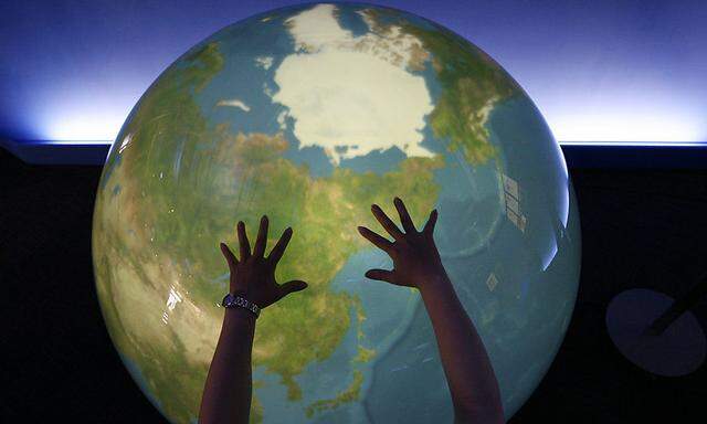 A visitor places her hands on a tangible earth, a digital globe, at an exhibition pavillion in Rusutsu town, northern Japan