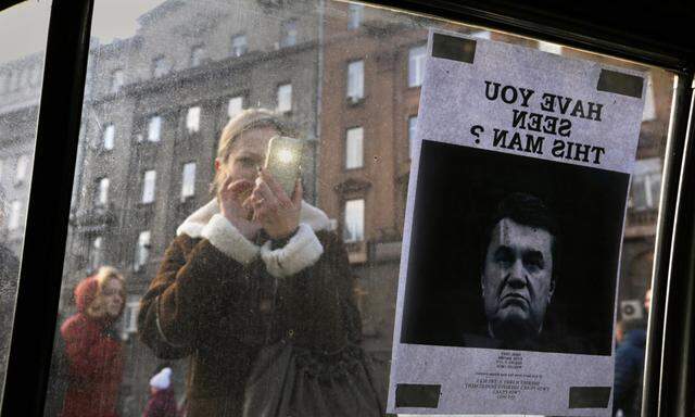 A woman takes photos of a ´Wanted´ notice for fugitive Ukrainian President Yanukovich near Kiev´s Independent Square