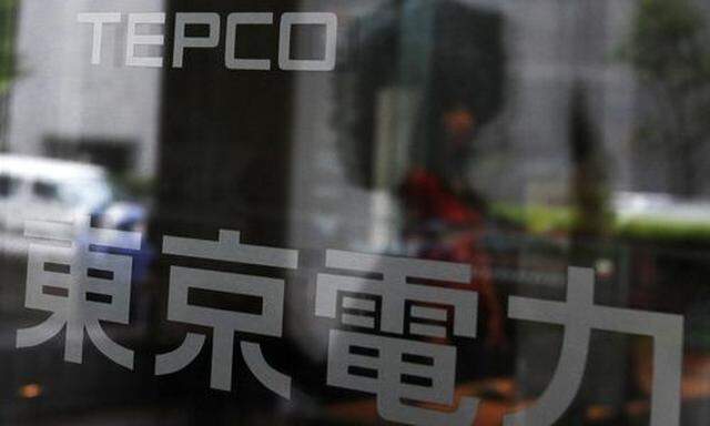 A woman walking into TEPCO headquarters building is reflected in the entrance door in Tokyo