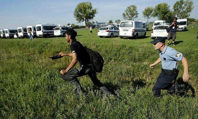 A migrant and a policeman run during a stampede to board a bus in Tovarnik