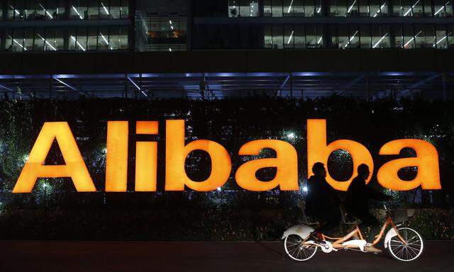 File photo of people riding a double bicycle past a logo of The Alibaba Group at the company´s headquarters on the outskirts of Hangzhou
