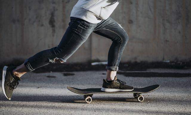 Side view of a boy with a skateboard on the street at dawn.