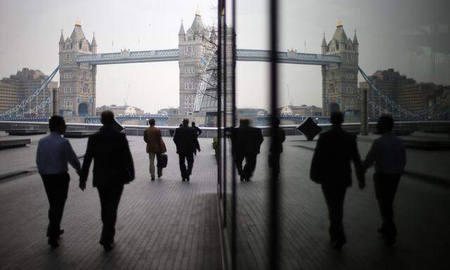 Pedestrians are reflected in glass fronted office buildings as they walk towards Tower Bridge on the south bank of the Thames, in central London