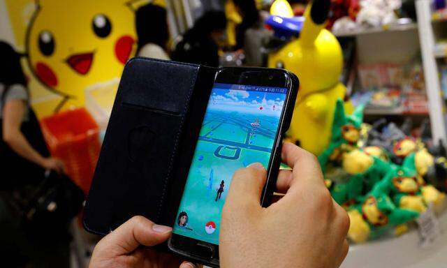 A man plays the augmented reality mobile game 'Pokemon Go' by Nintendo in front of a shop selling Pokemon goods in Tokyo