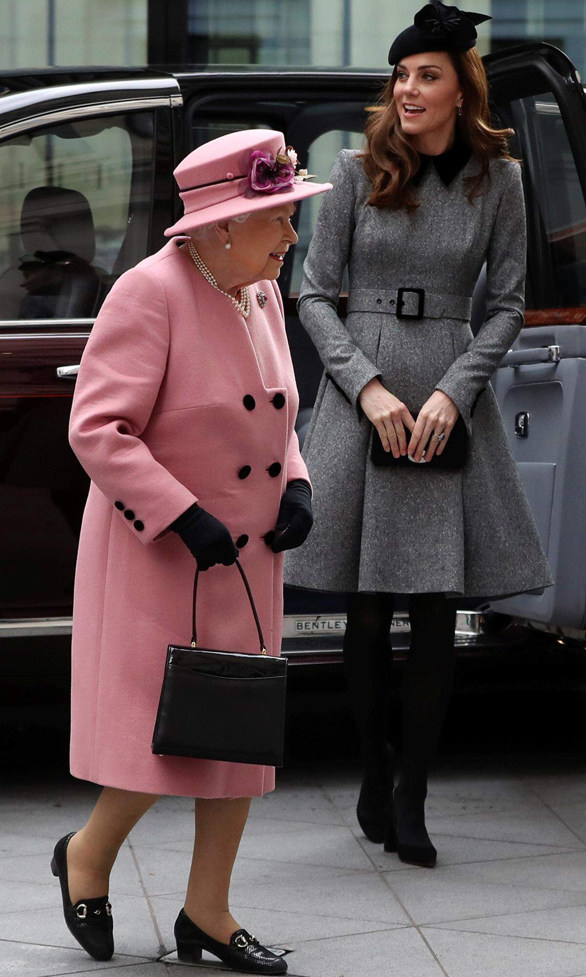 Fünf lange Jahre mussten ins Land ziehen, bevor Kate erneut die Ehre für einen Solotermin mit Queen Elizabeth II. hatte (zuletzt im Februar 2014 für einen Empfang im Buckingham Palace). Während sich die Queen bei ihrer Kleiderwahl für den gemeinsamen Besuch des King’s College in London von einem Punschkrapfen inspirieren ließ (Kaschmir-Mantel von Hofschneider Stewart Parvin), hielt sich die Frau von Prinz William in einem grauen Mantelkleid mit Taillengürtel und schwarzem Kragen von Catherine Walker, dunklen Strümpfen und Accessoires (Samtpumps von Gianvito Rossi, "Bayswater"-Clutch von Mulberry, Hut von John Lock, Ohrringe von Kiki McDonough) dezent im Hintergrund. Kate kennt eben die Rangordnung.