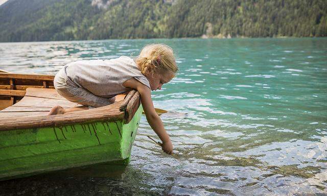 Austria, Carinthia, Weissensee, girl in rowing boat putting a stick in the water