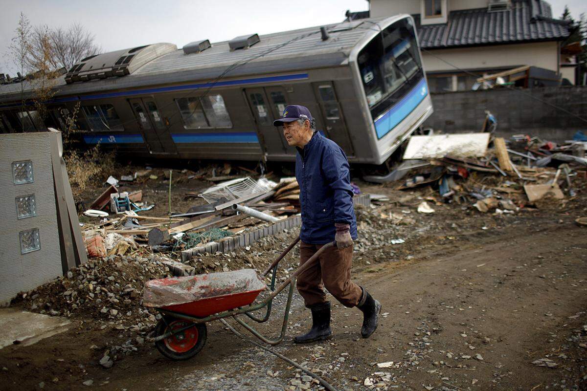 In Noribu bringt ein Mann vor dem Wrack eines angespülten Zuges den Schutt seines zerstörten Hauses weg. (31. März)