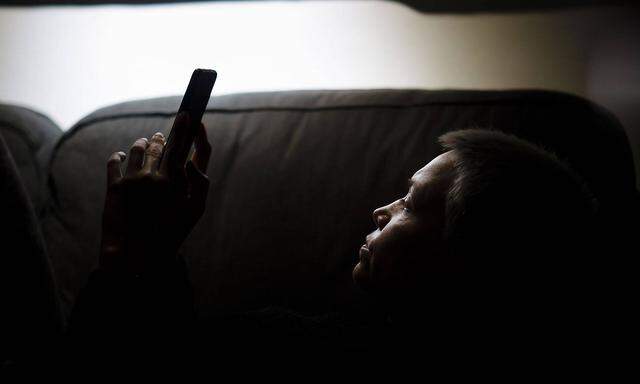 Symbolfoto zum Thema Einsamkeit und Isolation: Eine Frau sitzt nachts auf der Couch und schaut in ein Smartphone. Berli