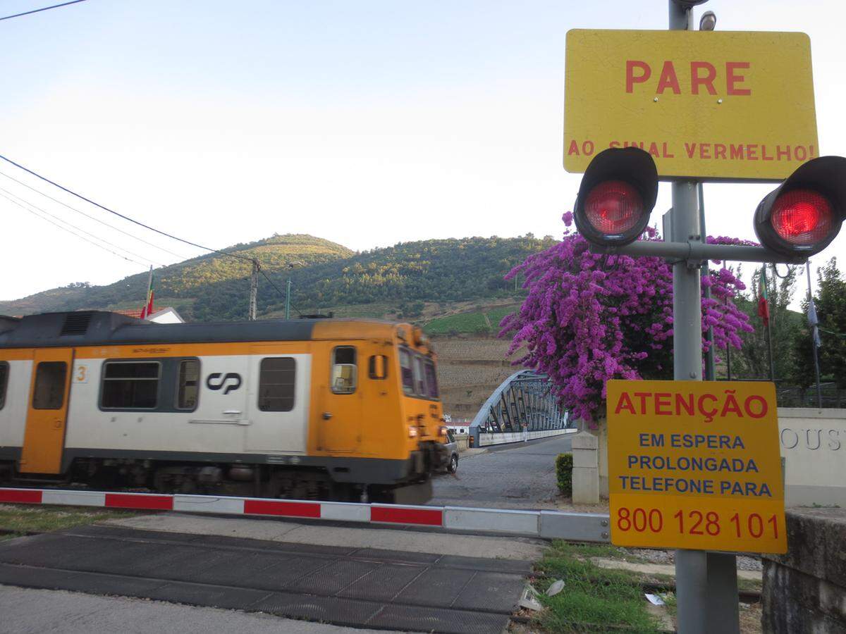 Der Zug nach Porto rast durch. Auf dem quadratischen Schild orangener Farbe steht eine Telefonnummer, die man anrufen soll, falls der Schranken überhaupt nicht mehr aufgeht. Sie ist aber besetzt.