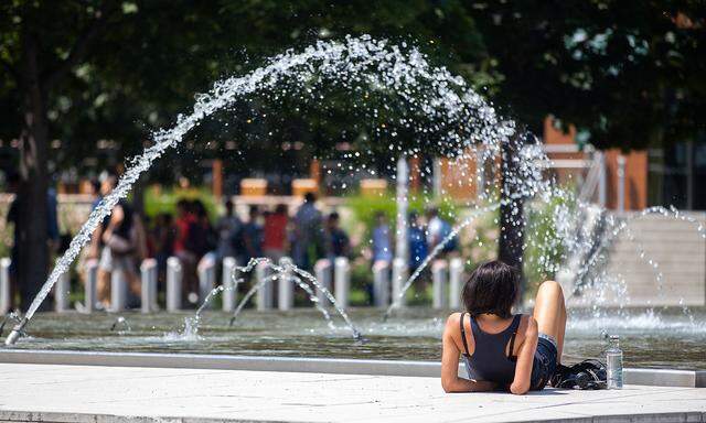 Themenbild: Eine Frau sucht Abkühlung bei einem Brunnen in Wien.