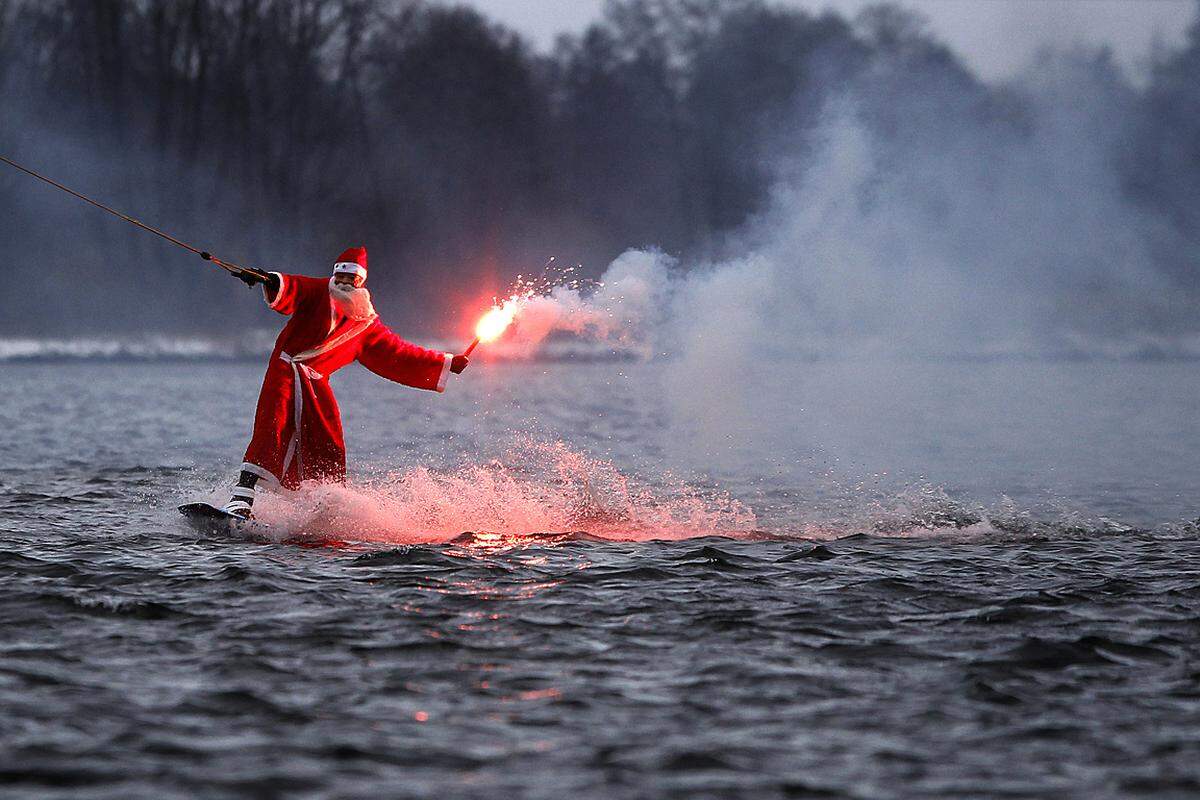 Hamburg, Deutschland. Santa und die Spaßgesellschaft. Auf einem See stimmt ein wakeboadender Weihnachtsmann mit einer brennenden Signalfackel auf das bevorstehende Fest ein.