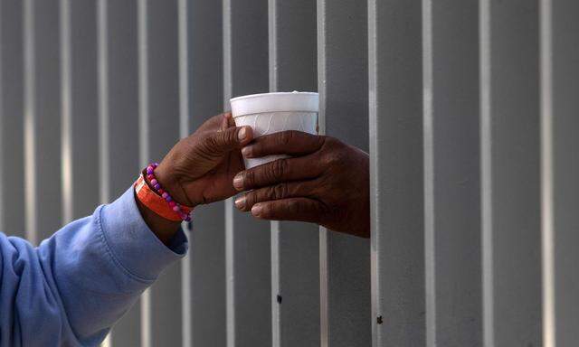 Im mexikanischen Grenzort Tijuana wird ein Kakao durch den Zaun einer Notunterkunft gereicht.