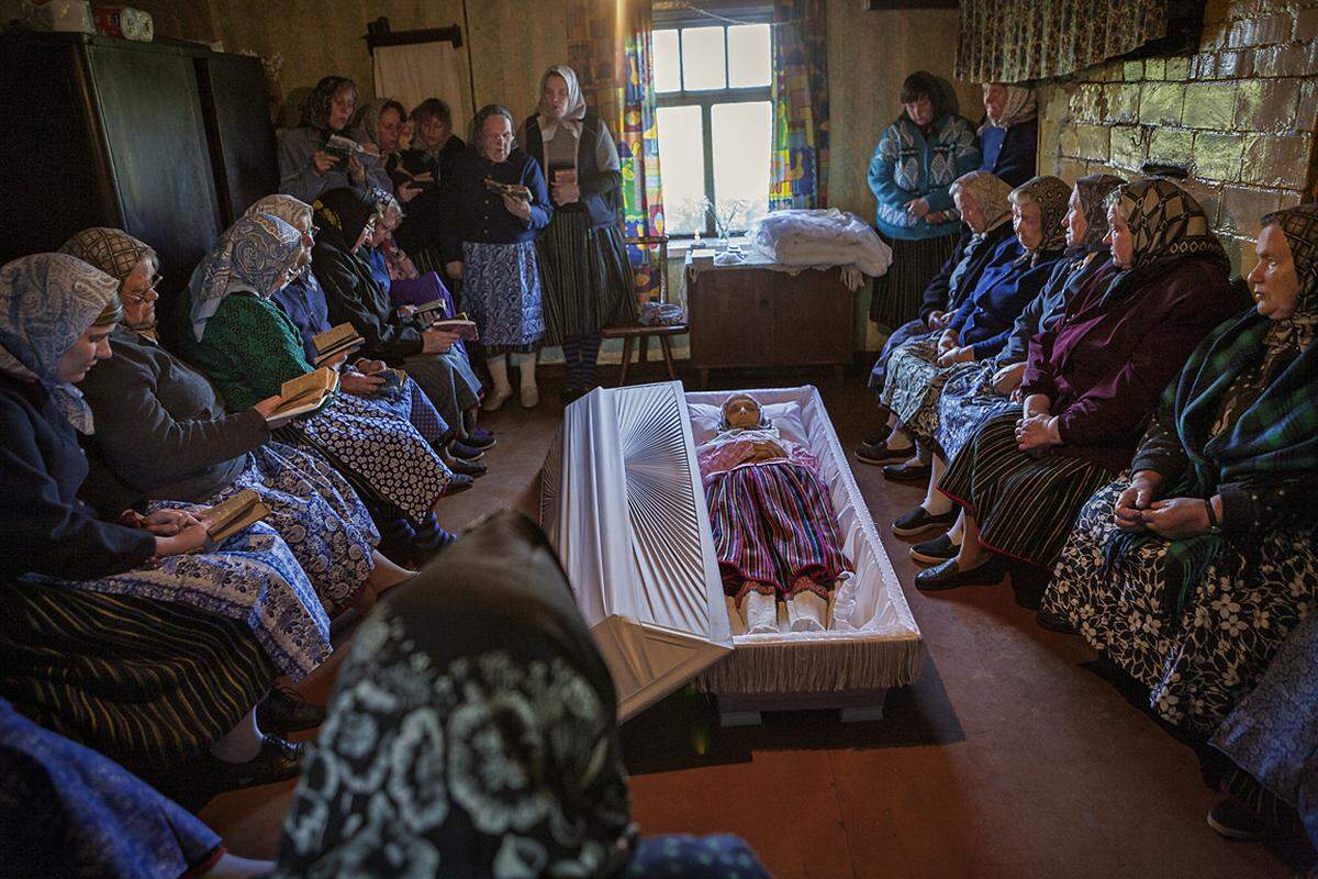 Koksi Leida, 2008, wenige Stunden nach ihrem Tod. "Ihre Nachbarn haben mir blaue Trauerkleidung gegeben und mich eingeladen, die Trauerfeier in der Küche zu fotografieren", schreibt die Fotografin. "Die Frauen aus dem Dorf versammelten sich um den Sarg, um zu beten und zu singen. Später kamen die Männer, um sich zu verabschieden. Dann wurde der Sarg geschlossen und Koksi Leida verließ mit den Füßen voran, wie es die Tradition verlangt, zum letzten Mal ihr Zuhause." Drinnen hätten die Frauen dann gekocht, draußen die Männer Wodka getrunken.