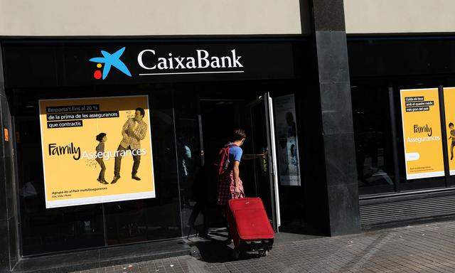 A man carrying a suitcase goes into a CaixaBank branch in Barcelona