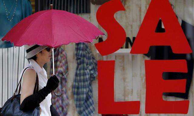 A woman holding her umbrella walks past a sales advertisement outside a luxury brand store at a shopping district in Tokyo