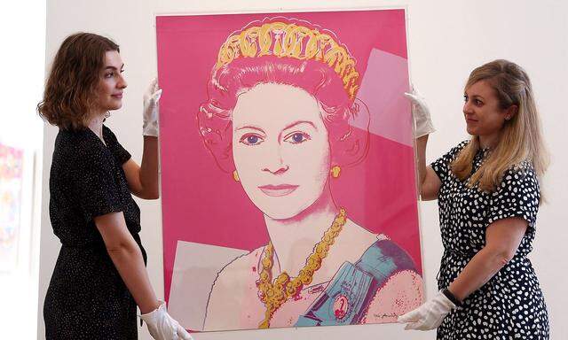 Gallery assistants pose with 'Queen Elizabeth II of the United Kingdom, from Reigning Queens (F. & S. 336) 1985' by Andy Warhol, at a photocall before the artwork is due to be auctioned at Phillips in London