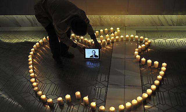 A man places an iPad displaying a picture of Steve Jobs around candles forming the logo of Apple Inc.