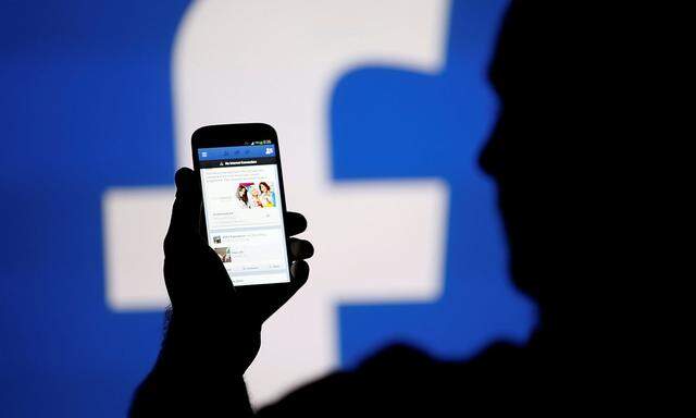 A man is silhouetted against a video screen with a Facebook logo as he poses with a smartphone in this photo illustration taken in Zenica