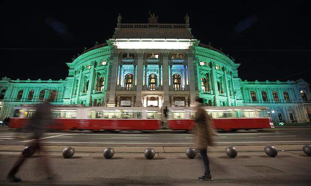 Two pedestrians pass by Burgtheater which is lit in green in celebration of St. Patrick´s day, in Vienna