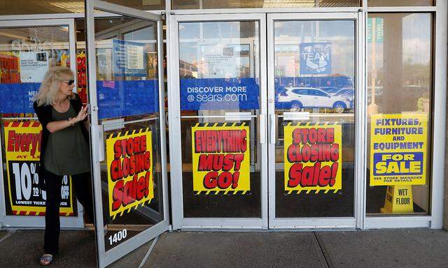 A woman walks out the door past signs advertising store closing signs Sears in New Hyde Park, New York