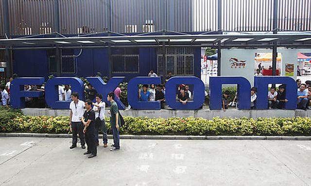 Company staff stand in front of the Foxconn logo at the entrance of the Foxconn complex in the southe