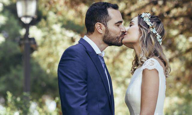 Happy bridal couple kissing in a park while holding hands model released Symbolfoto PUBLICATIONxINxG