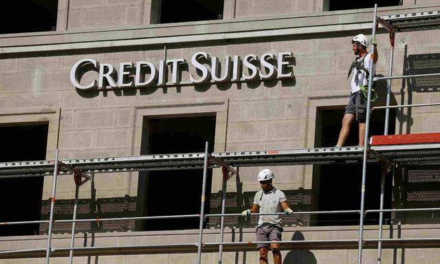 Construction workers stand on a scaffolding beside the logo of Swiss bank Credit Suisse at a construction site at the Bahnhofstrasse in Zurich