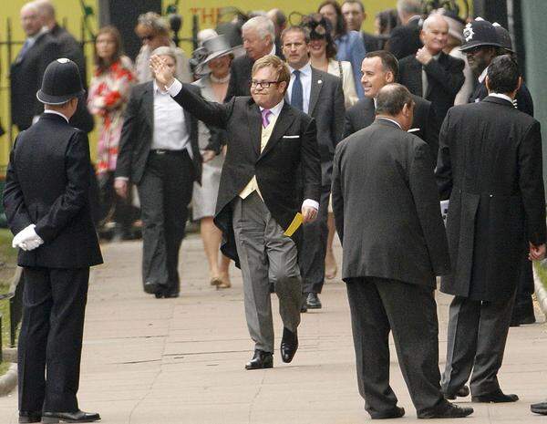 Musiker Elton John winkt beim Eintreffen vor der Kirche ein paar Fans zu. Etwas versteckt an seiner Seite: Gatte David Furnish.
