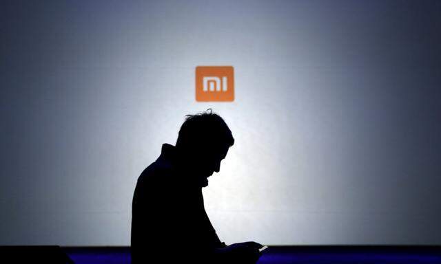 File picture of a man using his mobile phone in front of a screen showing a logo of Xiaomi in Beijing