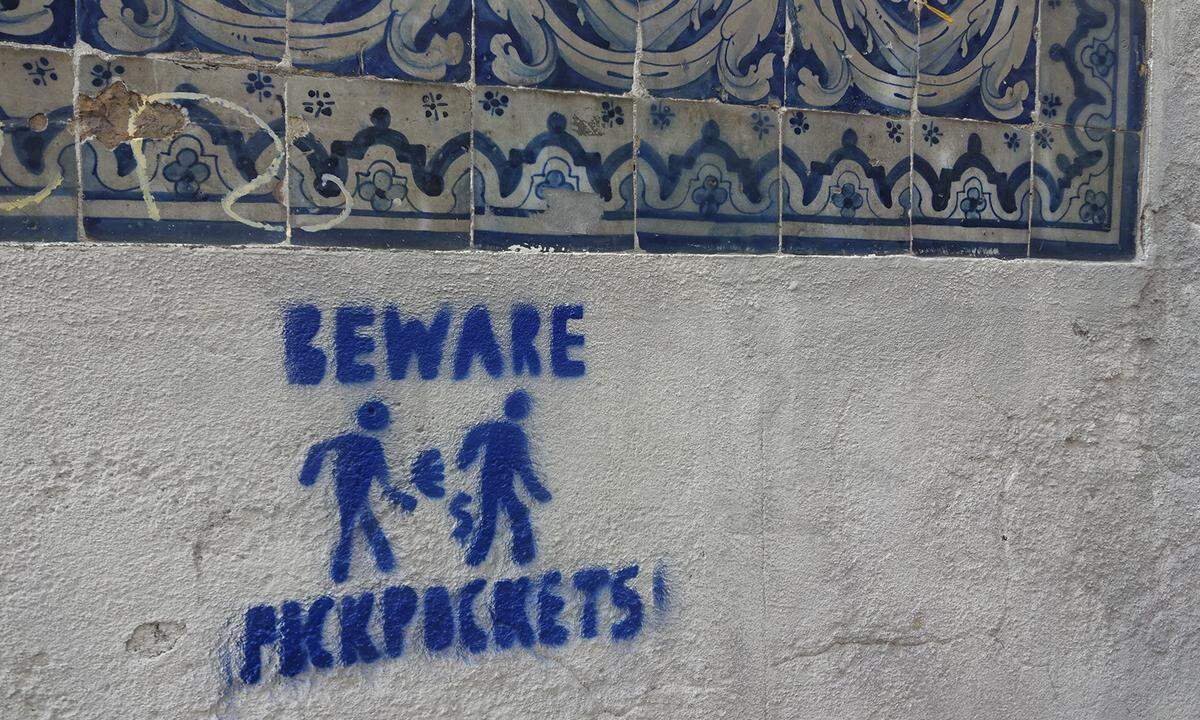 Unklar, ob die Stadtverwaltung solche Graffiti-Stempel anbringen lässt, oder ob es sich um eine private Initiative handelt. Fest steht, dass es sich bei Lissabon eine sichere Stadt mit einem höchstens durchschnittlichen Taschendiebaufkommen handelt. Dieses Bild zeigt auch einige Azulejos, glasierte Keramikfliesen, aus denen viele Lissaboner Hausfassaden gemacht sind.