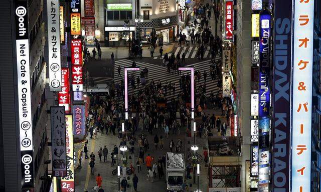 Passers-by walk under illuminated signboards at Kabukicho shopping and amusement district in Tokyo
