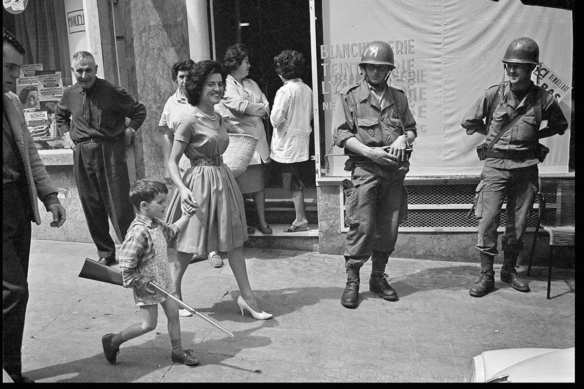 Algerien, 4. Mai 1962. Ein Bub und seine Mutter spazieren an französischen Soldaten am Bastille Palace in Oran vorbei.