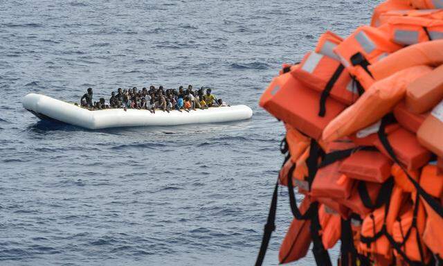 Symbolbild: Flüchtlinge in einem Schlauchboot blicken auf Rettungswesten  