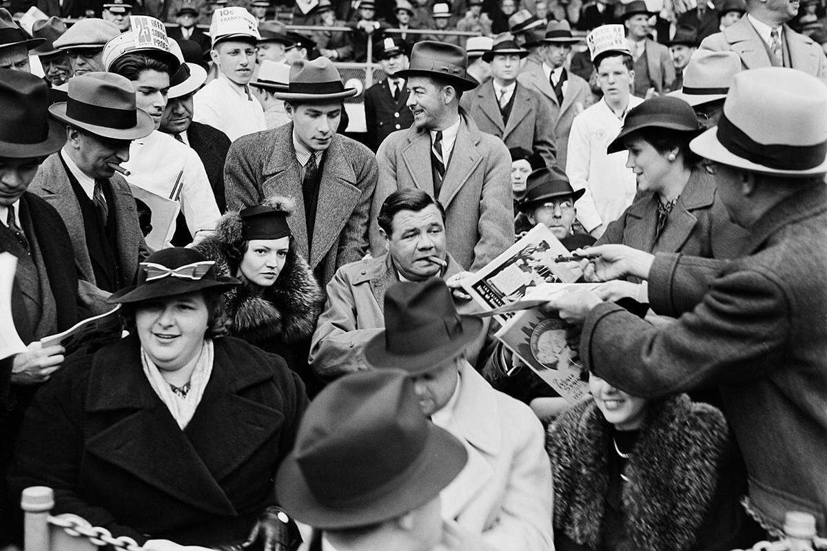 Baseball-Legende Babe Ruth, der Mann mit der Zigarre, erhält ein Programm beim ersten Spiel der Saison 1936. Links neben ihm ist seine zweite Frau Clare, links vorne die Sängerin Kate Smith.