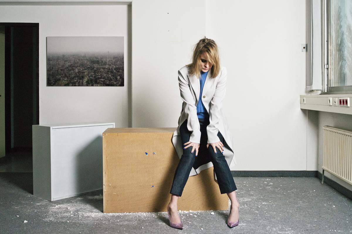 Hinter Bernadette Heerwagen an der Wand hängt ein Bild mit dem Titel „Untitled (Tokio)“, das 2008 fotografiert wurde und im Film zu sehen ist. Sie trägt hier einen Pullover von Prada, einen Mantel von Boss, eine Hose von Hermès und Heels von Stuart Weitzman.