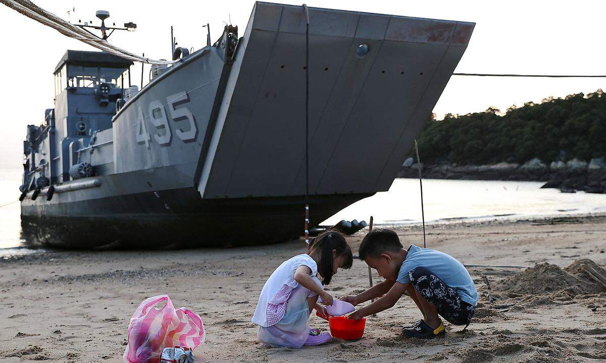 Kinder spielen im Sand in der Nähe eines Versorgungsschiffs der taiwanesischen Marine am Strand auf der Insel Nangan im Matsu-Archipel in Taiwan.