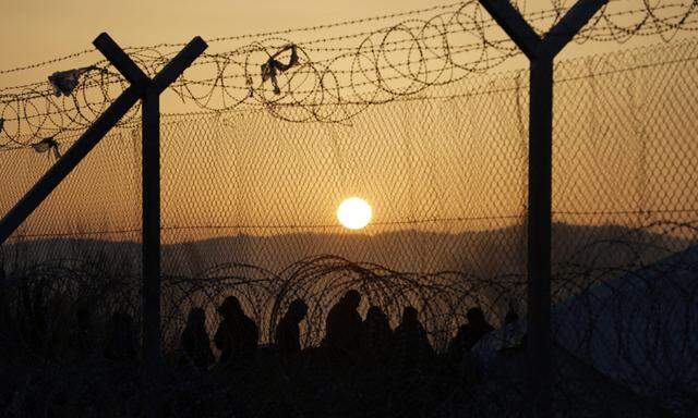 Migrants stand behind a border fence at the Greek-Macedonian border