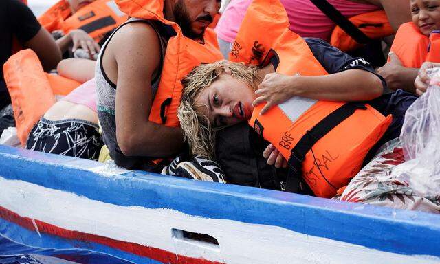 Migrants on a wooden boat wait for the Italian Guardia Costiera in the Mediterranean Sea