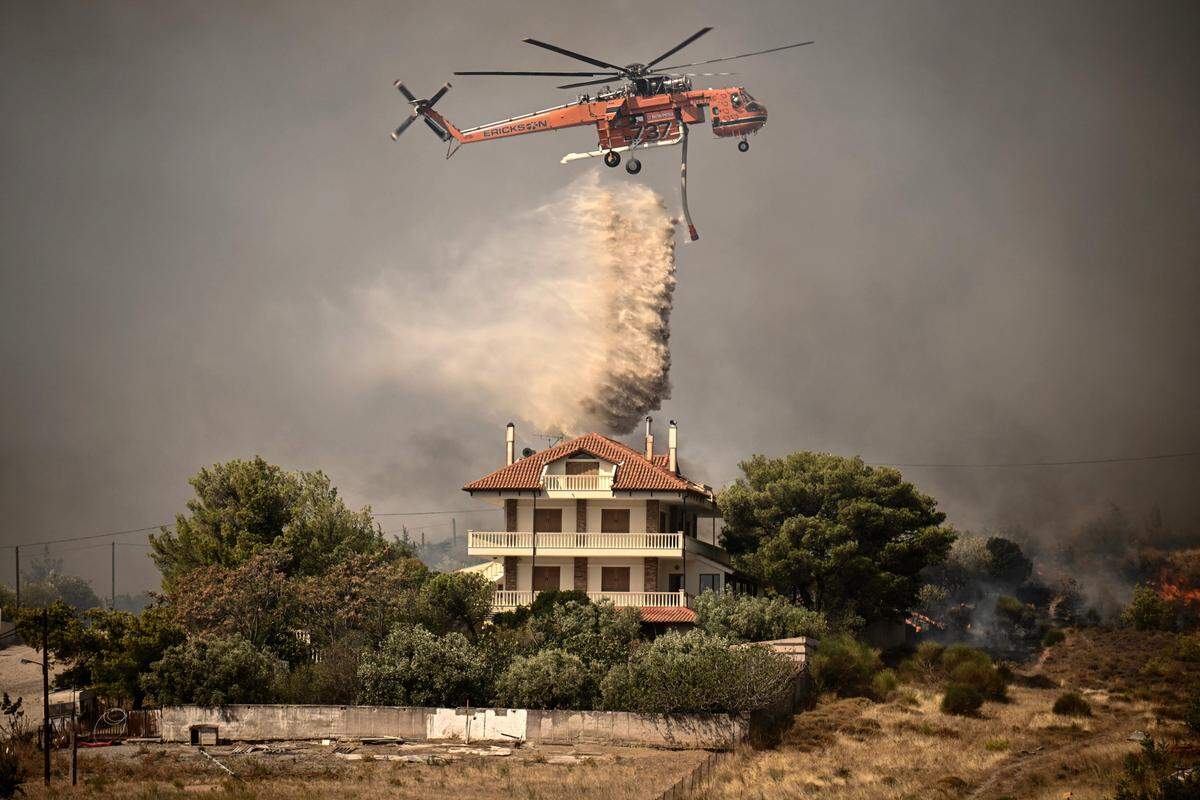 23. August. Ein Löschhubschrauber wirft während eines Waldbrandes in Acharnes, nördlich von Athen, Wasser über einem Haus ab.