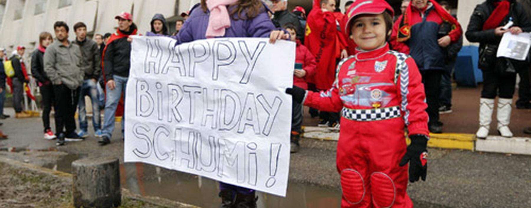 Kids celebrate with a placard the 45th birthday of seven-times former Formula One world champion Michael Schumacher in front of the CHU hospital emergency unit in Grenoble, French Alps