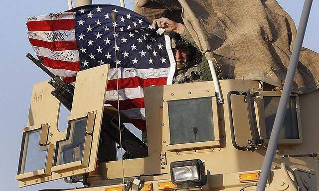 A U.S. Army soldier waves an American flag after crossing into Kuwait during the last convoy out of Iraq