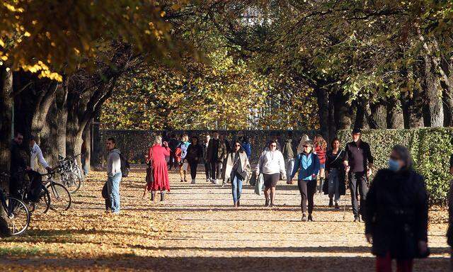 Passanten genieszen den warmen und sonnigen Herbsttag bei einem Spaziergang durch den herbstlichen bunten Hofgarten der