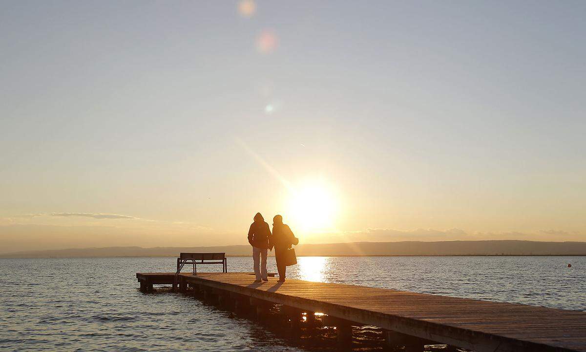 A couple walks on a dock at Lake Neusiedl (Neusiedlersee) in Weiden