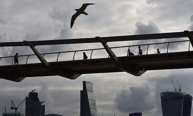 Workers cross the Millenium Bridge with the City of London seen behind, in London