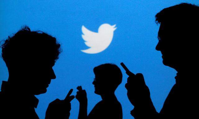FILE PHOTO: People holding mobile phones are silhouetted against a backdrop projected with the Twitter logo in Warsaw