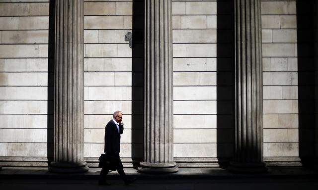 A man speaks on his phone on a sunny morning as he walks past the columns of the Bank of England in the City of London