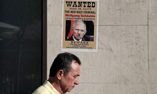A man walks past a poster depicting a defaced image of German Finance Minister Wolfgang Schaeuble on the wall of a Eurobank branch in Athens