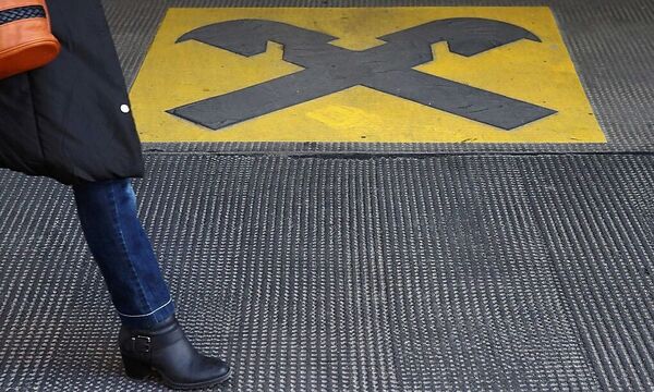 A woman walks by a Raiffeisen logo painted on the ground in front of an office building in Vienna