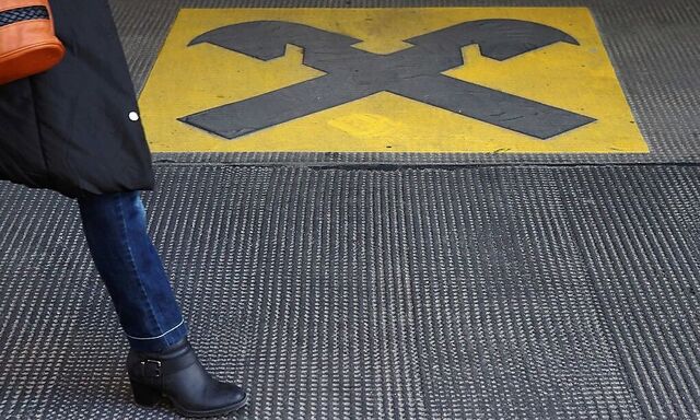 A woman walks by a Raiffeisen logo painted on the ground in front of an office building in Vienna